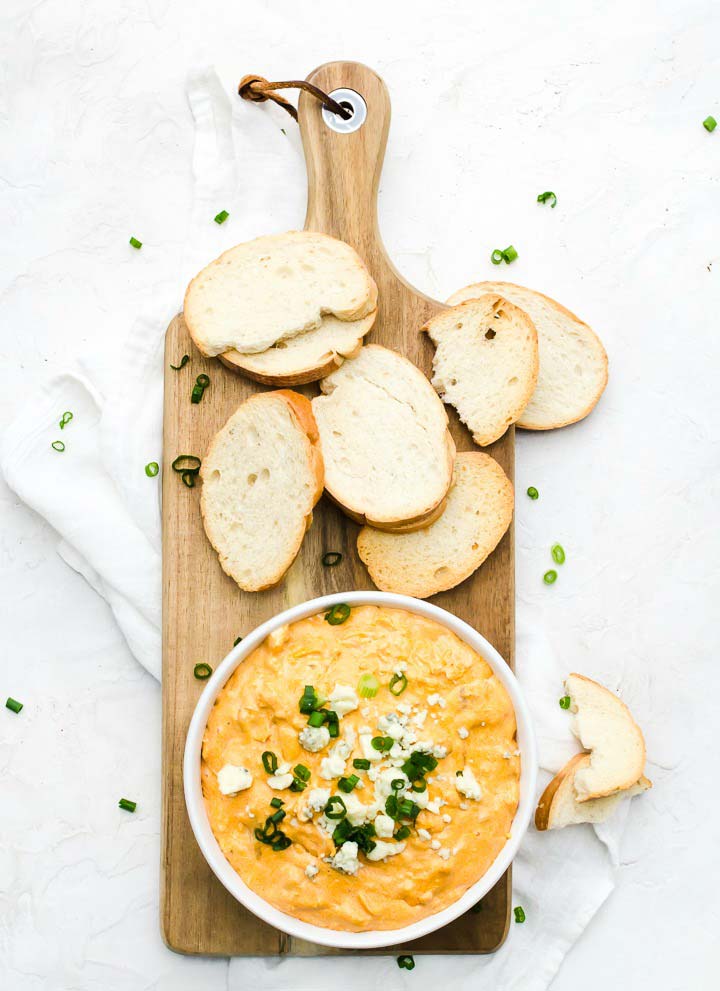 bowl of buffalo chicken dip and crostini for dipping on wood serving platter