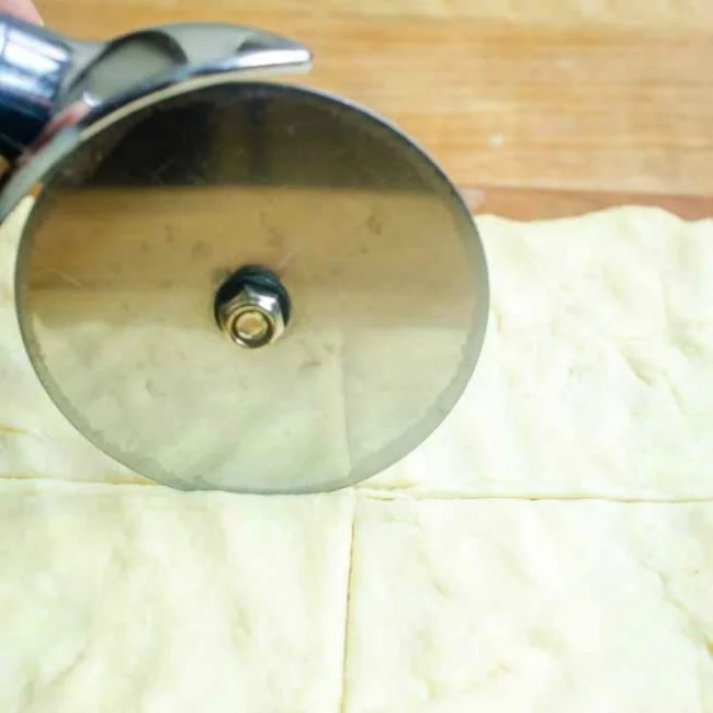 cutting crescent roll dough into squares with a pizza cutter
