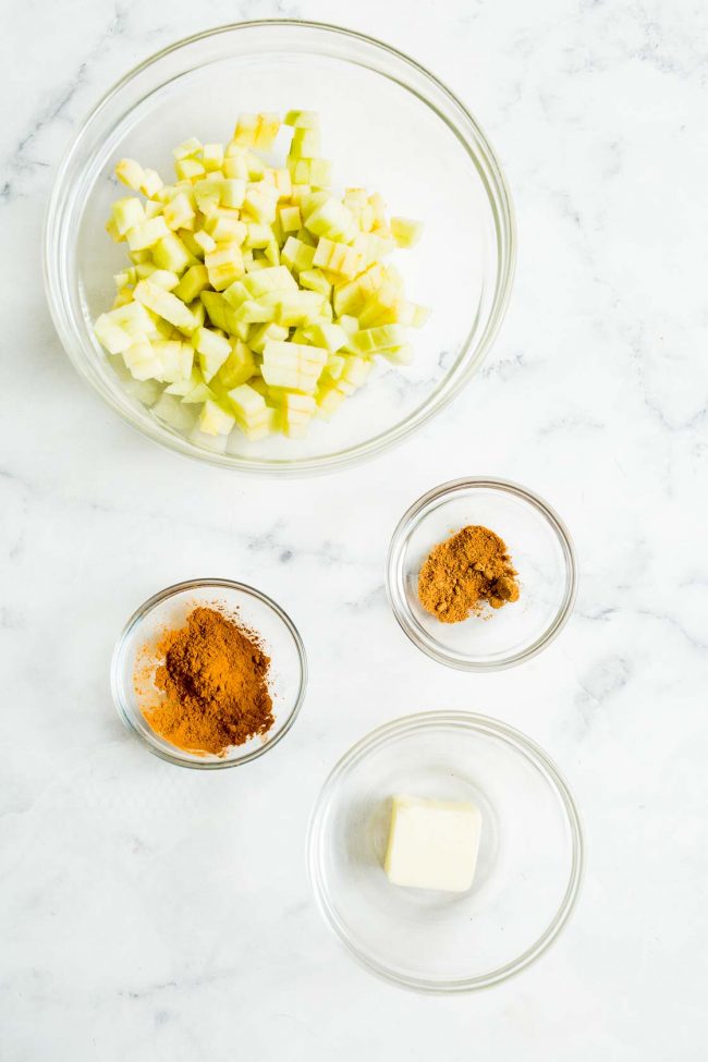 An overhead view of diced apples, cinnamon, nutmeg, and butter.