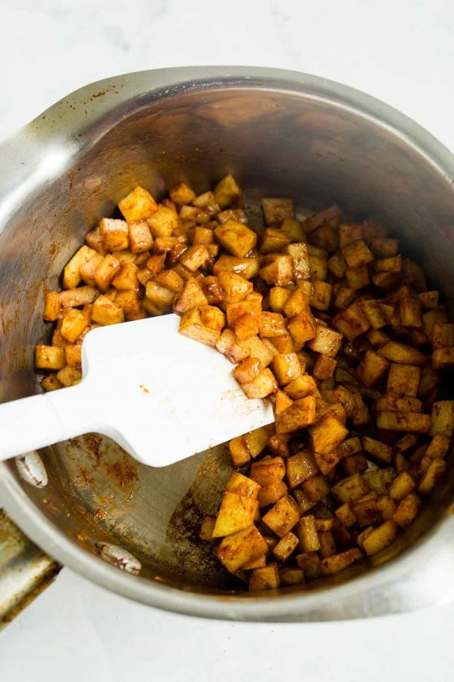 An overhead view of sautéed diced apples in a silver stove pot.