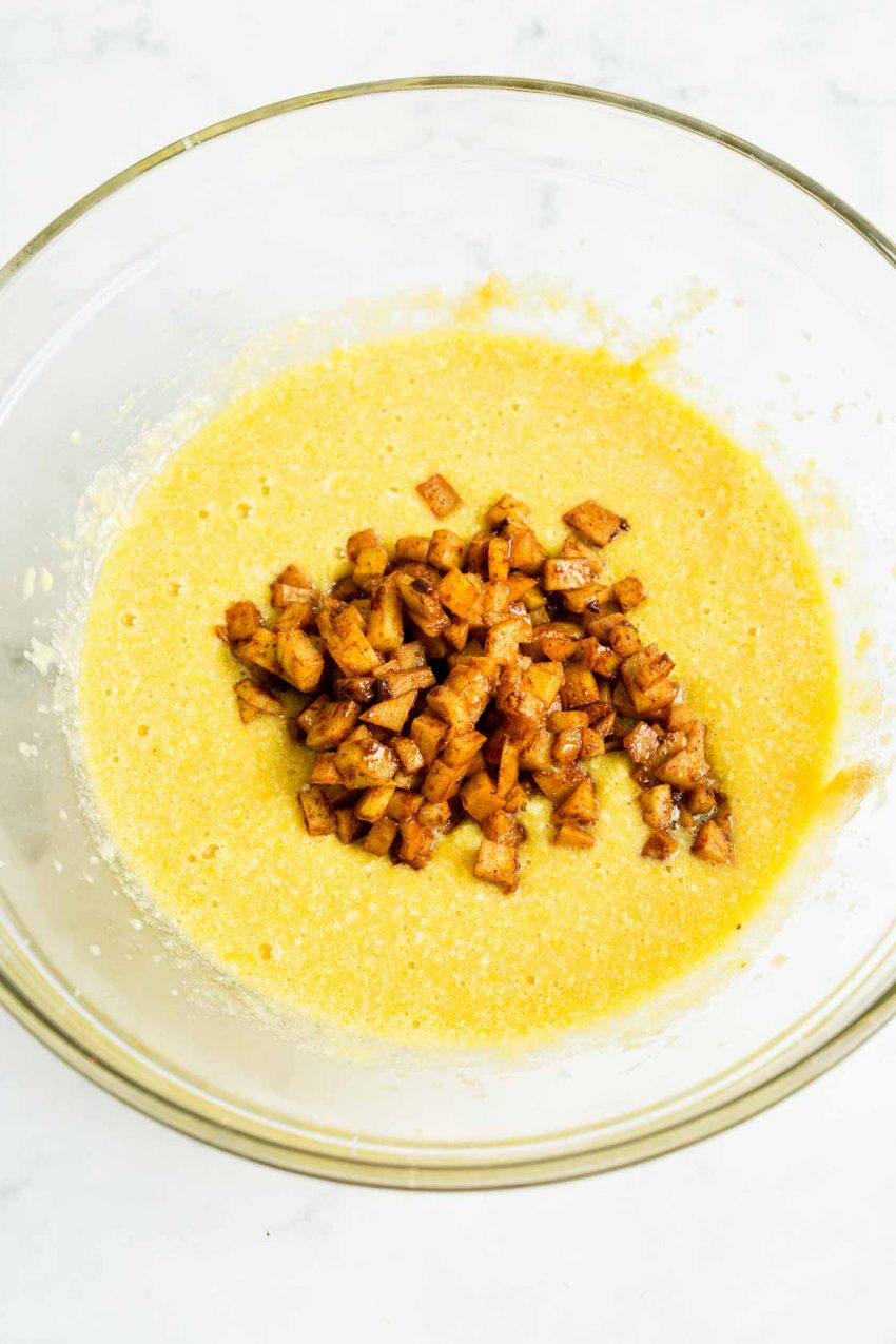 A bowl of wet ingredients and sautéed apples required for apple cinnamon donuts.