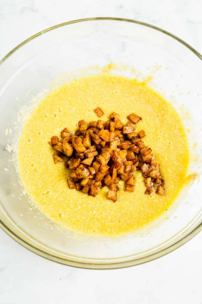 A bowl of wet ingredients and sautéed apples required for apple cinnamon donuts.