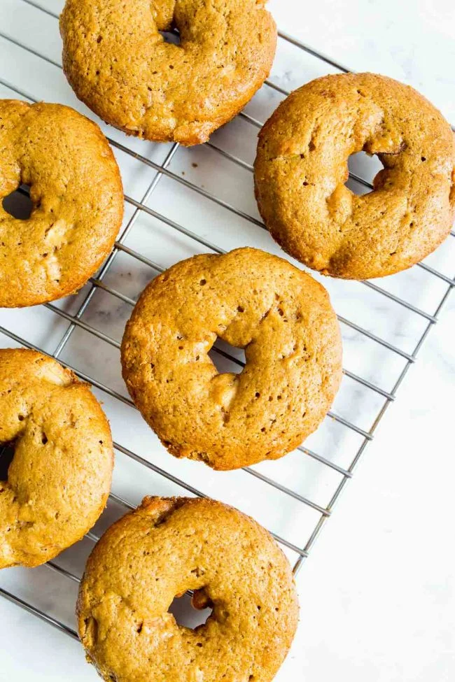 An overhead image of freshly baked apple cinnamon donuts on a cookie sheet.