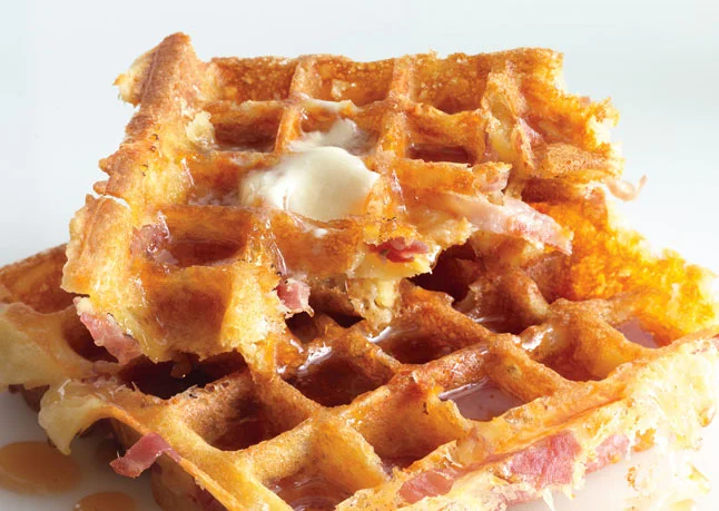 Ham and Cheddar Waffles topped with a pat of butter and maple syrup