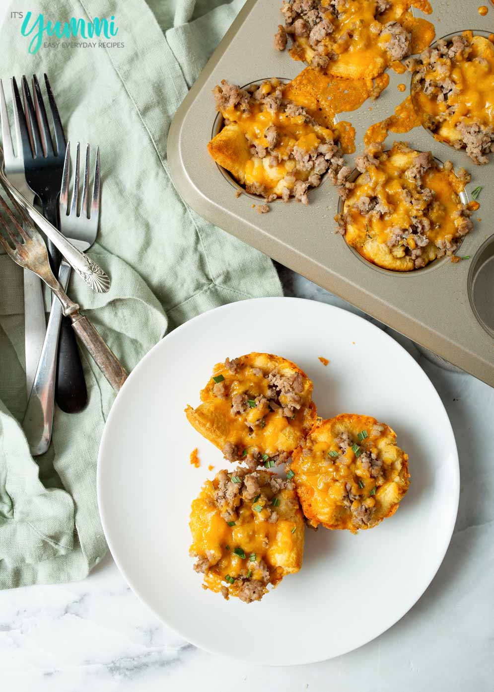 Three Sausage Biscuits displayed on white plate and in muffin pan in upper right corner
