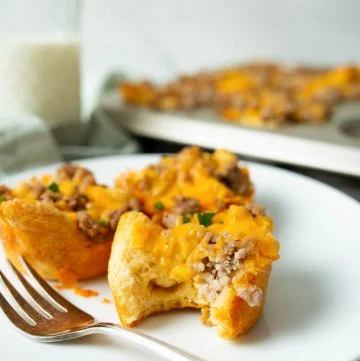 Cheesy Sausage Biscuit on white plate with bite taken out of with glass of milk in background