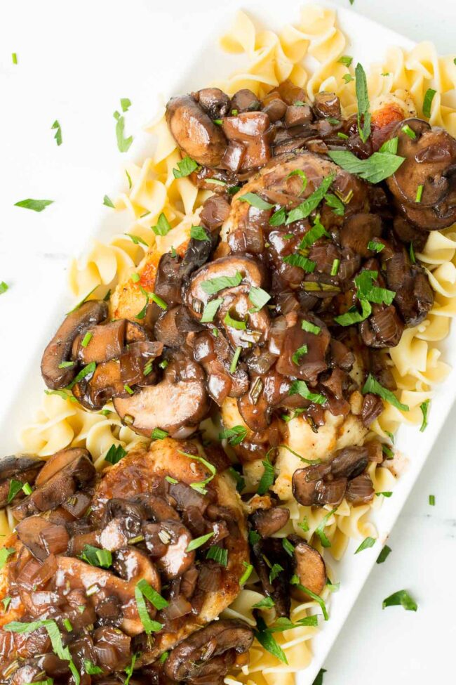 an overhead image of a white platter with mushroom chicken bourguignon and fresh parsley