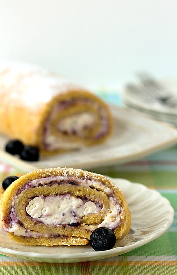 This roll cake features fresh blueberry preserves and whipped cream tucked inside of moist sponge cake. It's one of my favorite easy summer desserts that I want to make all year long! It's such an easy cake recipe, too. Let your kids help you make it! slice of Blueberries and Cream Cake
