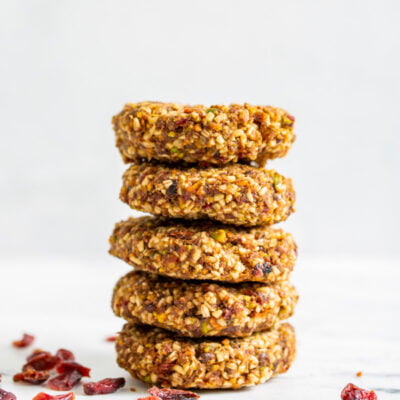 A close up side view of a stack of no bake pistachio oat cookies surrounded by dried cranberries