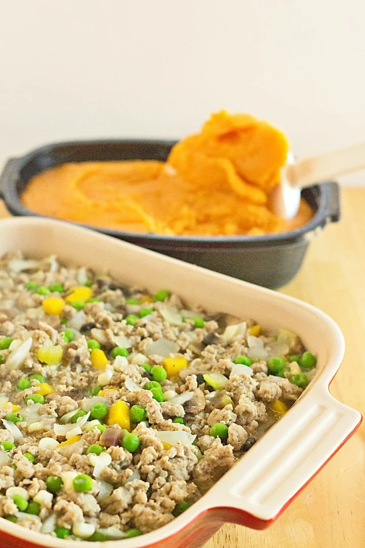 Easy Sweet Potato Shepherd's Pie Casserole - Ground turkey and fresh vegetables, cooked until tender and topped with rich, creamy mashed sweet potatoes. This is a taste of Thanksgiving that can be enjoyed any time of the year! Recipe from @itsyummi dish of sweet potato shepherd's pie filling with mashed sweet potatoes behind it
