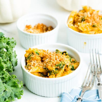 creamy turkey pumpkin pasta in white bowls set next to kale and white pumpkins