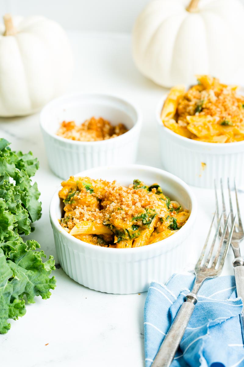 creamy turkey pumpkin pasta in white bowls set next to kale and white pumpkins