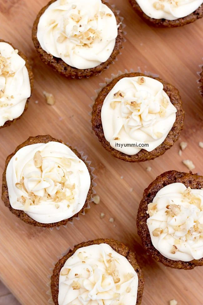 carrot cake cupcakes topped with cream cheese frosting, sitting on a wood platter
