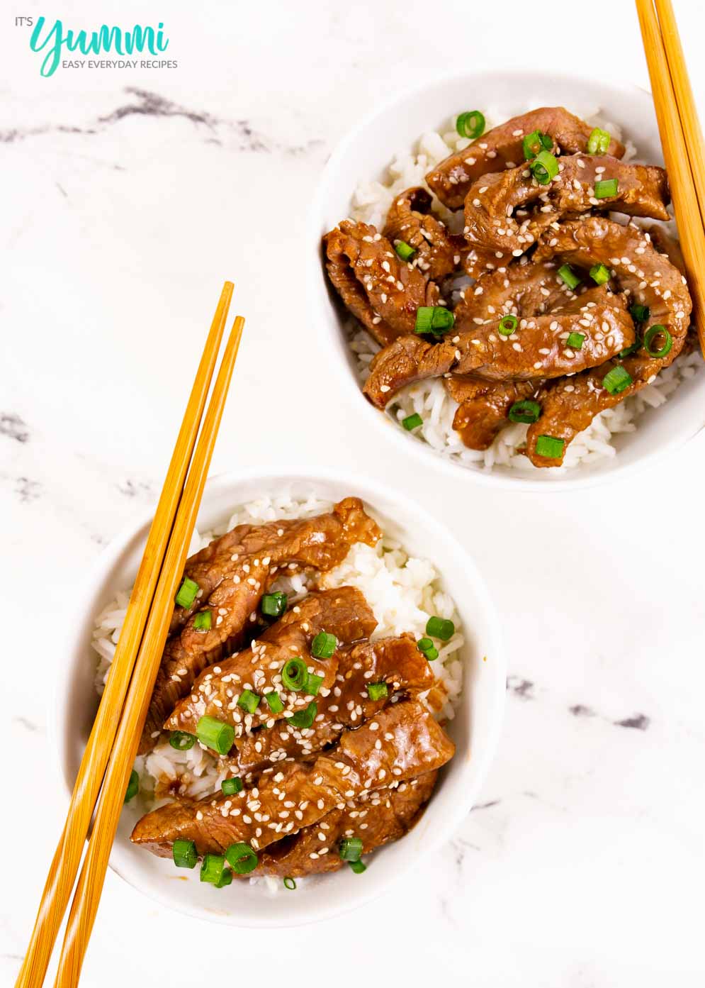 Two bowls on a white backdrop with rice and mongolian beef strips with chopsticks resting on sides of bowls
