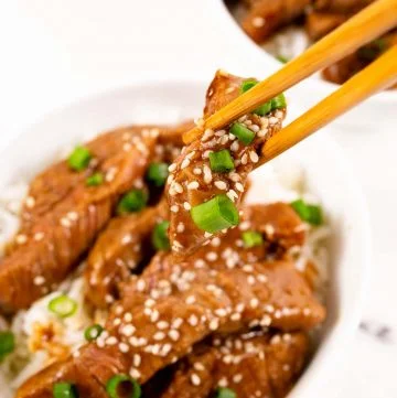 Close-up shot of chopsticks holding a piece of pf changs mongolian beef strip with scallions and sesame seeds on top