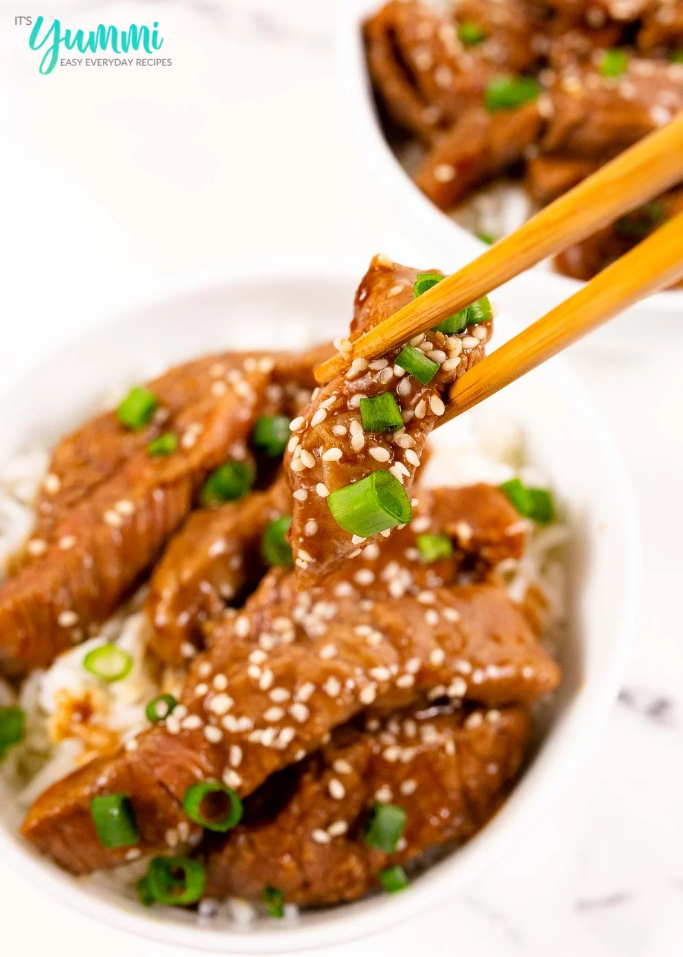 Close-up shot of chopsticks holding a piece of pf changs mongolian beef strip with scallions and sesame seeds on top