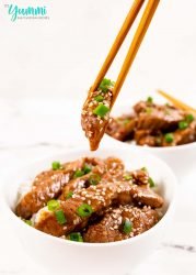 Chopsticks focus as they lift a piece of mongolian beef out of a bowl with whitebackground