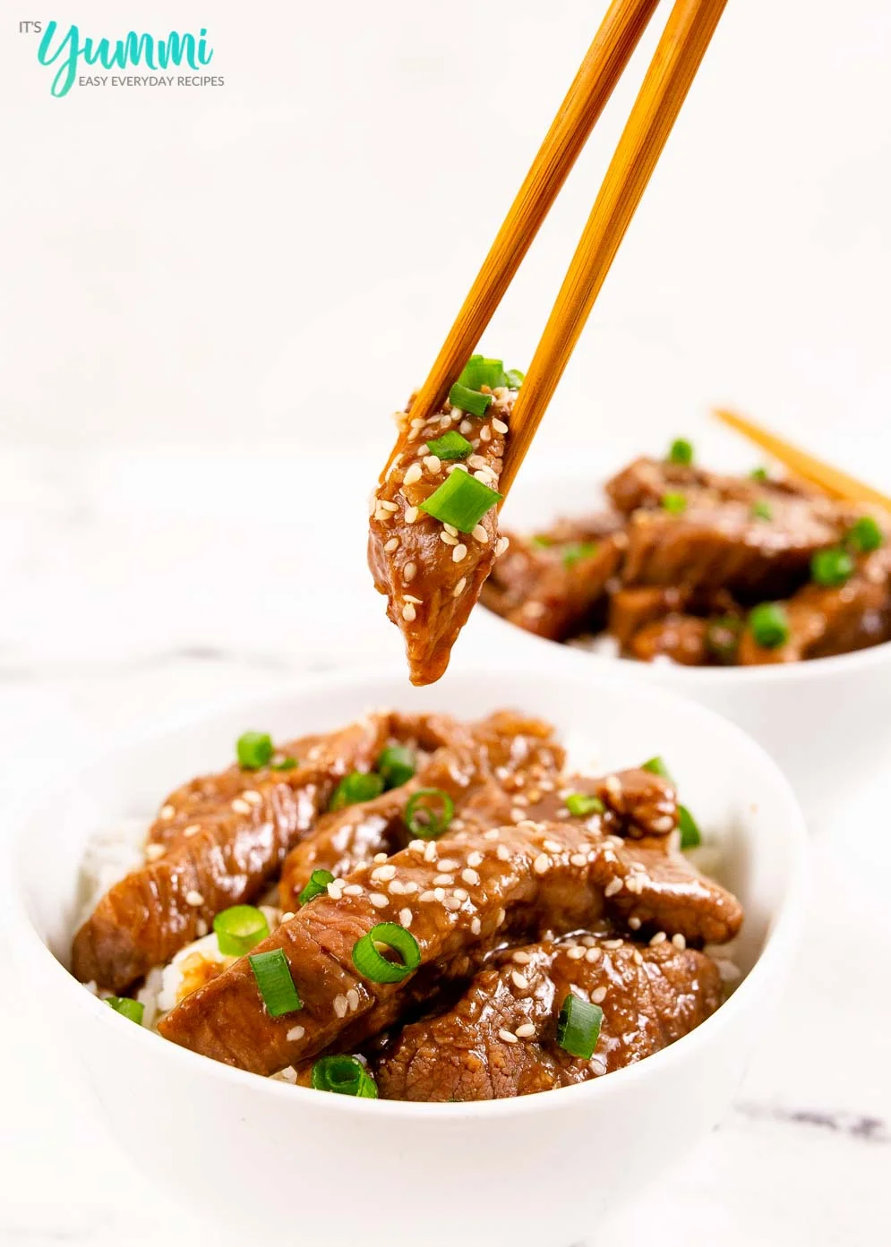 Chopsticks focus as they lift a piece of mongolian beef out of a bowl with whitebackground