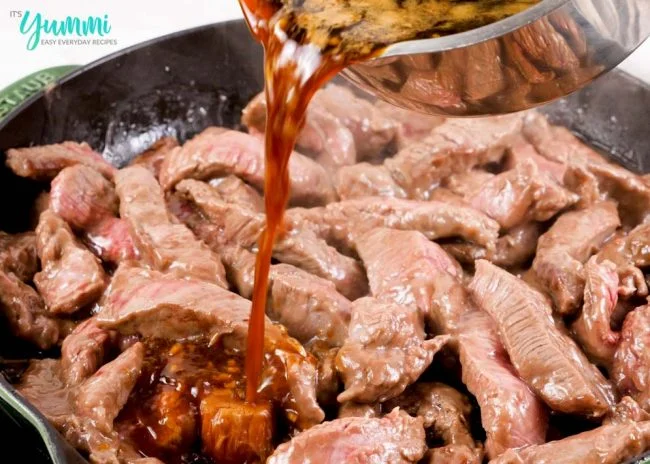 Close-up shot of pouring sauce over mongolian beef strips in skillet