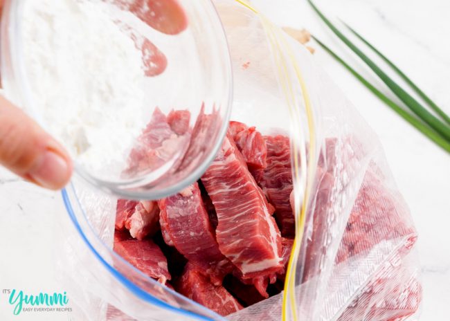 Beef strips in a plastic bag being tossed in cornstarch