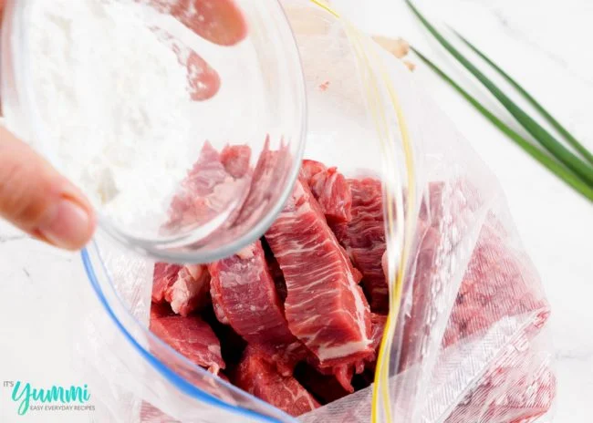 Beef strips in a plastic bag being tossed in cornstarch