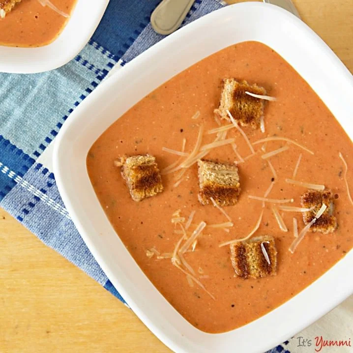 square white soup bowl filled with Homemade creamy Tomato Soup with Grilled Cheese Croutons and Parmesan Cheese