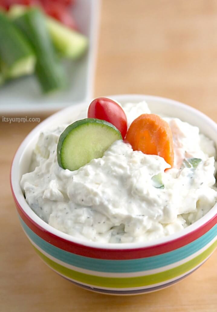 bowl of creamy dill cucumber yogurt dip with fresh raw veggies dipped into it.