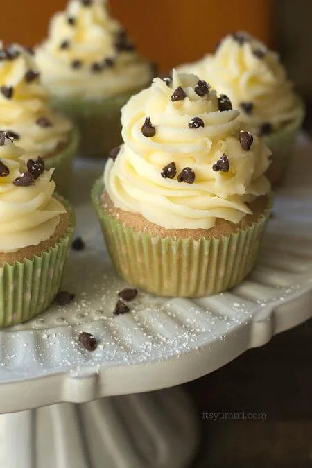 Cannoli cupcakes are inspired by the popular Italian dessert. Moist cinnamon cupcakes, topped with fluffy mascarpone buttercream and a sprinkling of chocolate chips and powdered sugar. Recipe on itsyummi.com