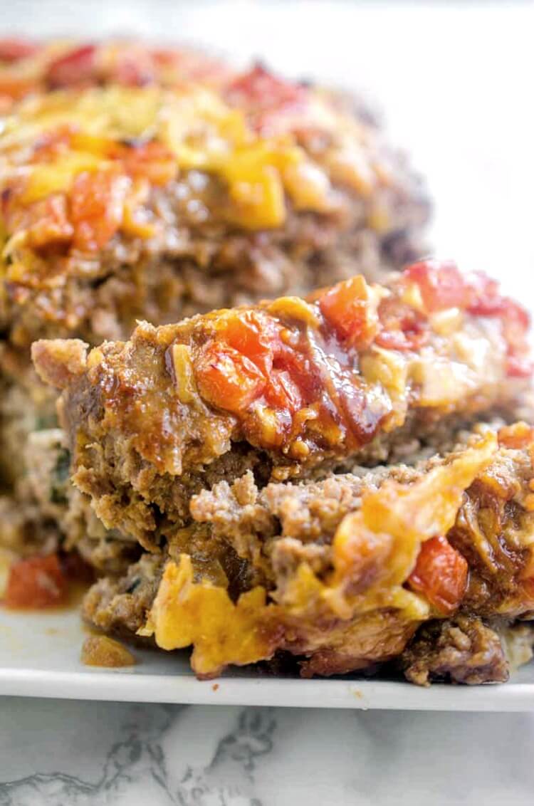 Veggie stuffed meatloaf is the best meatloaf I've ever eaten - complete comfort food. Ground pork and beef meatloaf is stuffed with spinach, onions, and cheese, then topped with barbecue sauce, tomatoes, and more cheese! #meatloaf #recipe #dinner