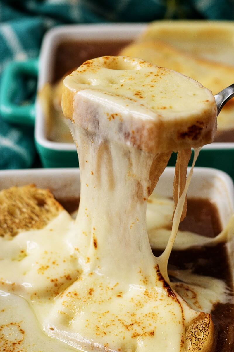 photo of French onion soup in a bowl, with a cheese covered crouton being pulled up from the bowl.