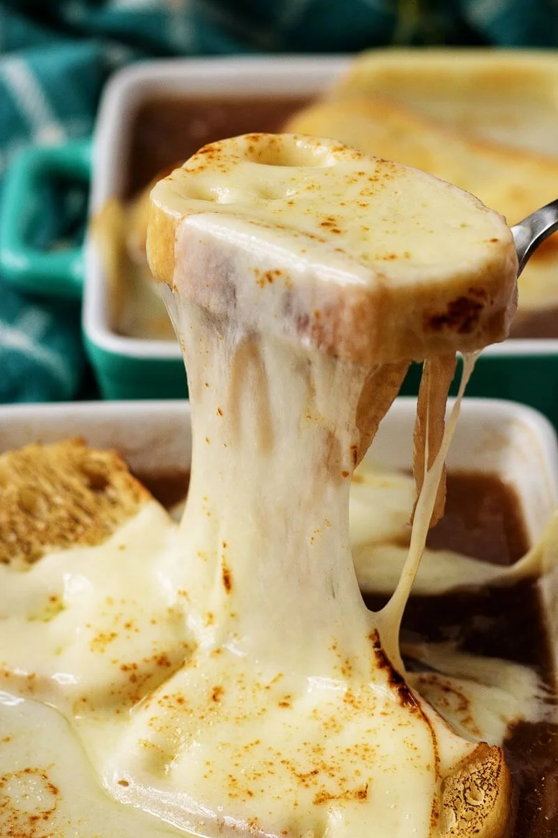 photo of French onion soup in a bowl, with a cheese covered crouton being pulled up from the bowl.