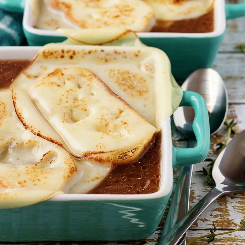 2 bowls of French onion soup with melted cheese on top and two spoons next to them.