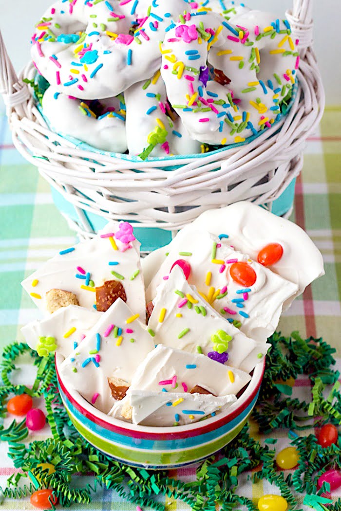 pastel colored, striped bowl sitting on Easter grass, surrounded by jelly beans. In the bowl is homemade Easter candy bark