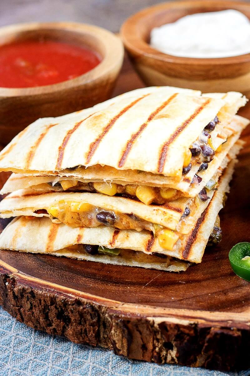 Vegetarian quesadillas will be a welcome entree for a meatless Mexican dinner or lunch. Each Tex Mex quesadilla is stuffed with a spicy corn and black bean mixture and cheese.This quesadilla recipe is ready to eat in 20 minutes. Includes Weight Watcher's friendly options - substitutions noted in the recipe. #Mexican #WeightWatchers #recipe #quesadilla #appetizer #vegetarian #meatless vegetarian quesadillas filled with spicy corn and black bean mixture and cheese on a natural wood serving platter (with bark exterior)
