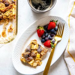 French toast bake with apples and dried cherries on white plate next to fresh berries