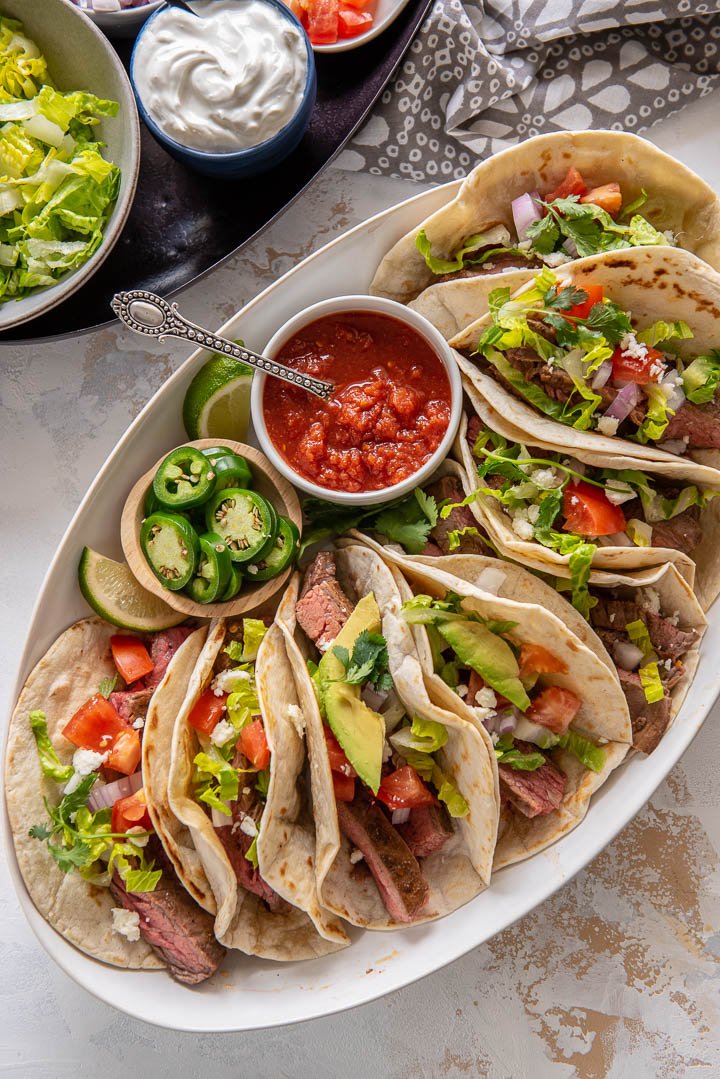 Pan seared steak is the perfect way to cook steak in the oven for this steak taco recipe. It makes for the juiciest best steak tacos! #tacorecipes #steaktacos #pansearedsteak platter of oven cooked steak tacos