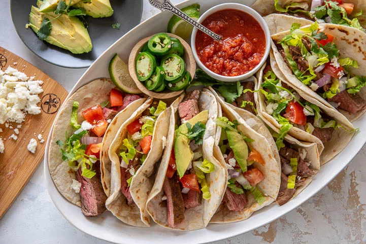 marinated steak tacos on a platter with taco toppings