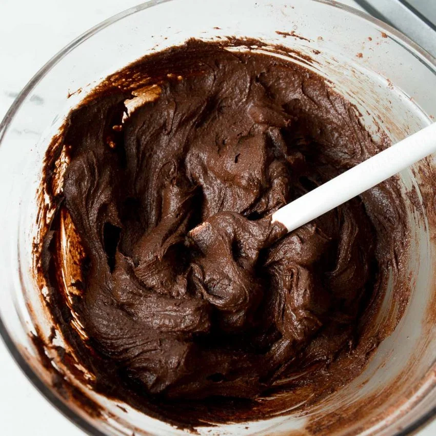 A glass bowl of brownie batter with a white spatula.
