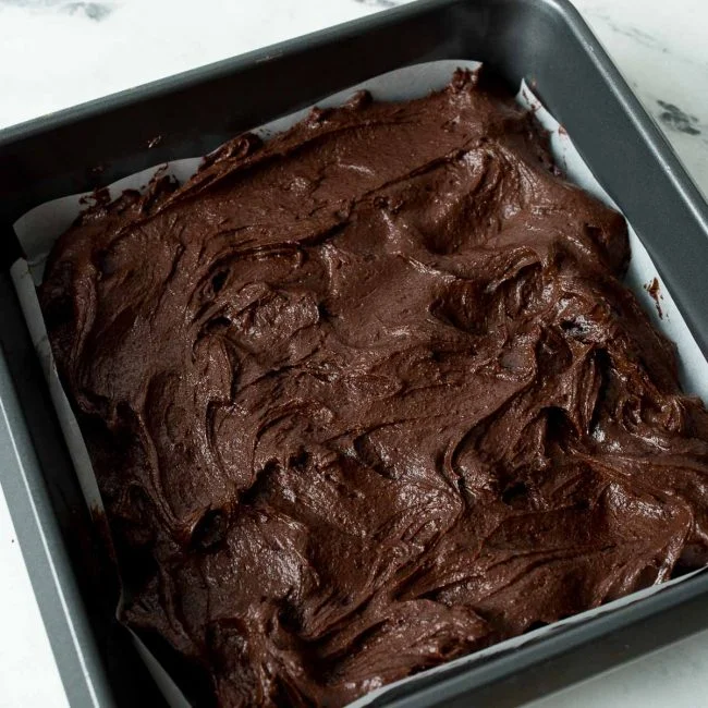 A 9x9 inch non-stick pan lined with parchment paper, filled with brownie batter.