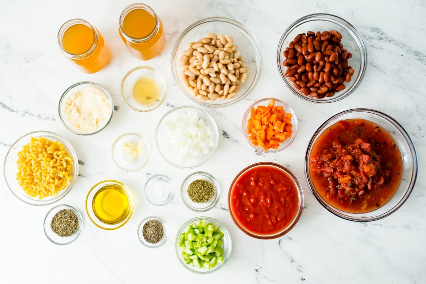 Image of all the ingredients required for vegetarian minestrone soup in individual glass bowls on a white marble top.