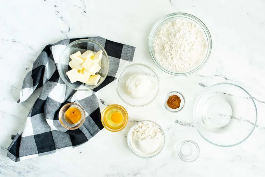 Individual ingredients for homemade crust are laid on a white marble countertop.