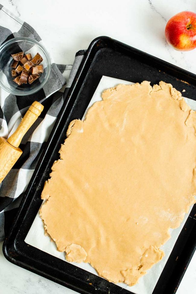 Pie dough is rolled out onto a baking sheet lined with parchment paper.