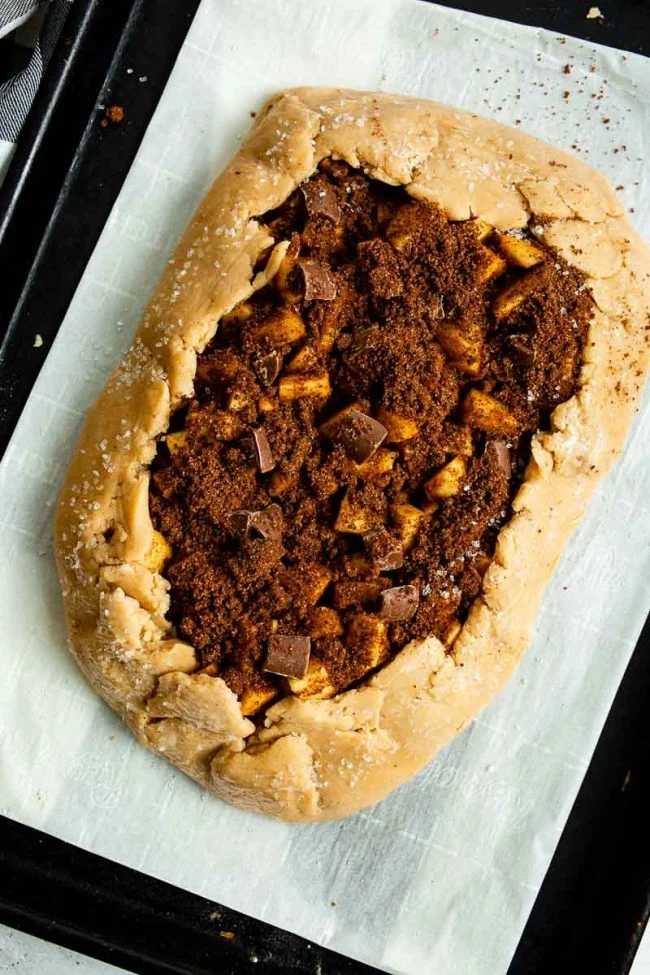 The edges of the pie crust are folded up in a rustic fashion, slightly over the apple galette filling.