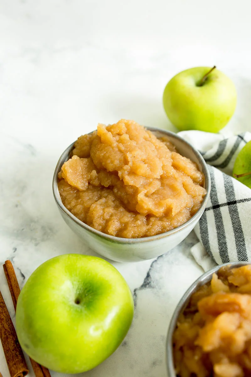 two bowls of chunky slow cooker applesauce with apples around