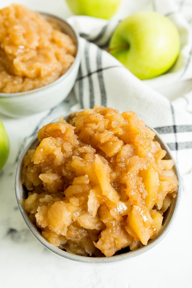 A close up image of chunky applesauce with green apples in the background