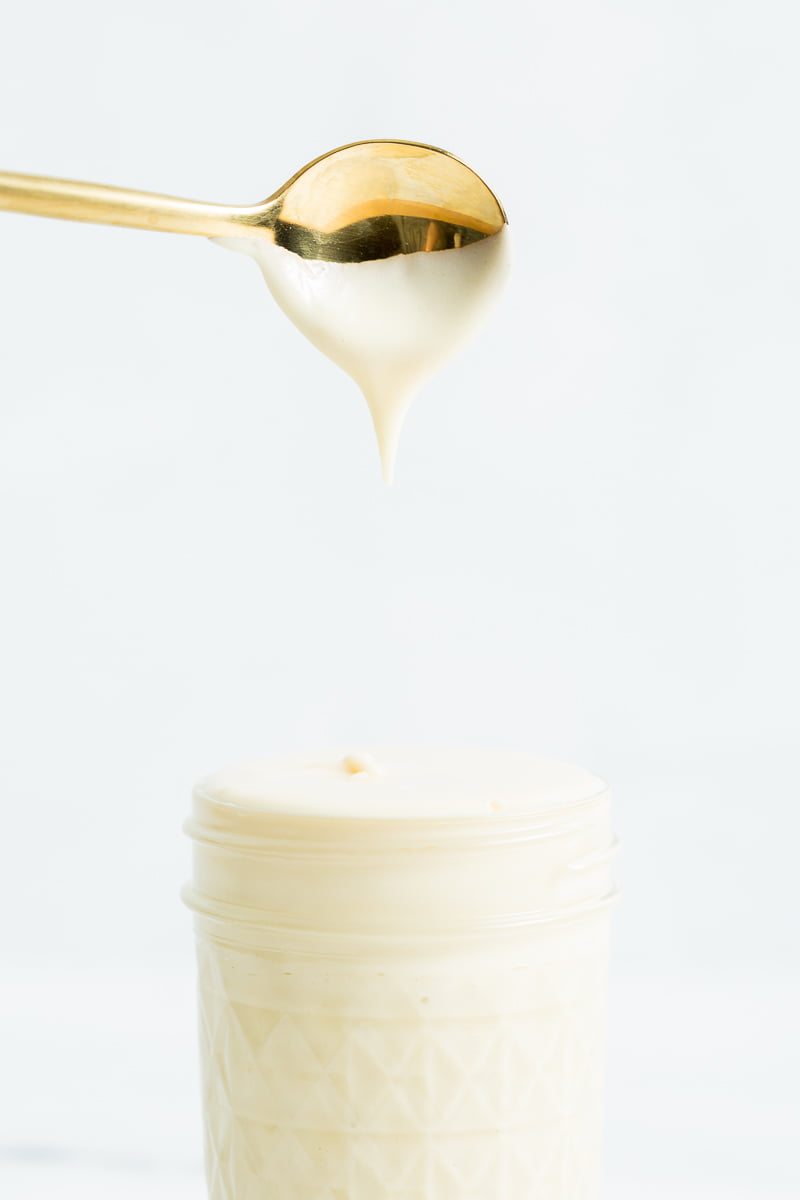 Small mason jar of sweetened condensed milk under a dipped gold spoon. 