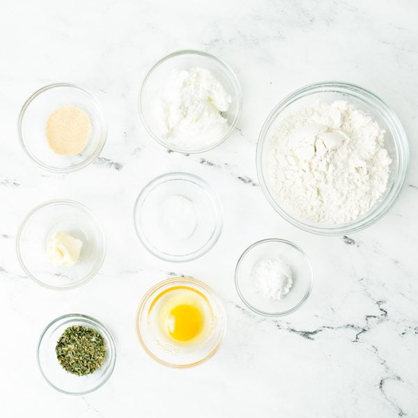 Ingredients for gluten free breadsticks on a white marble countertop in individual glass bowls. 