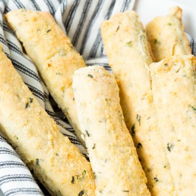 A closeup of homemade gluten-free italian breadsticks wrapped in a blue and white stripped cloth towel.