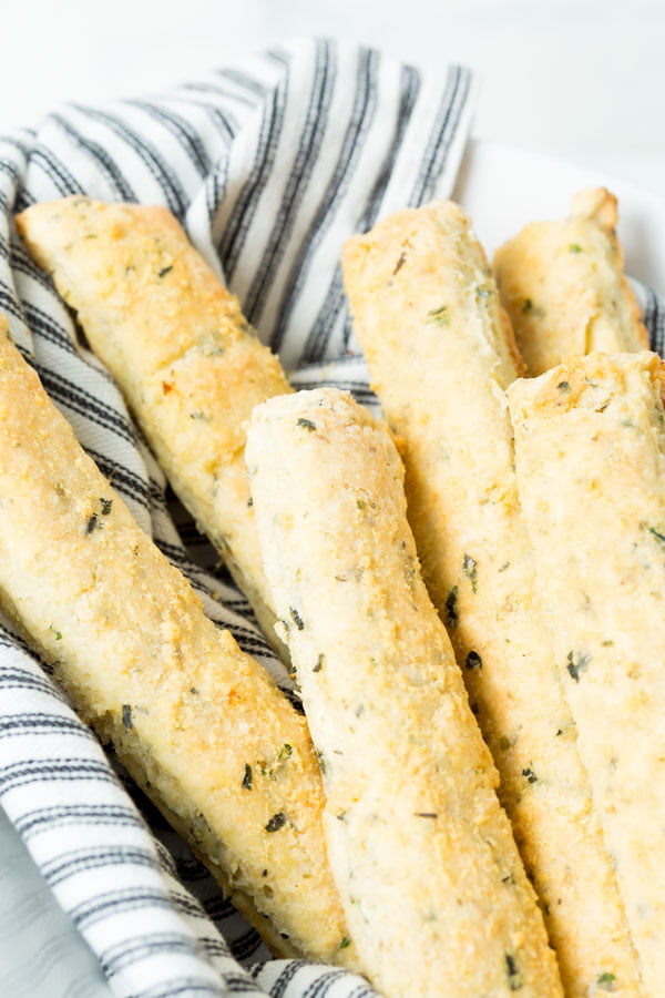 A closeup of homemade gluten-free italian breadsticks wrapped in a blue and white stripped cloth towel.