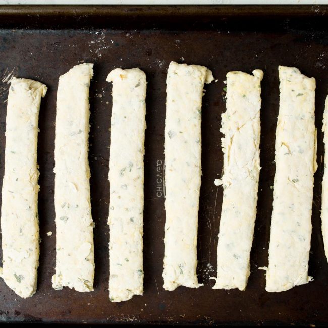 8 rustic breadsticks pre baked on a baking sheet.